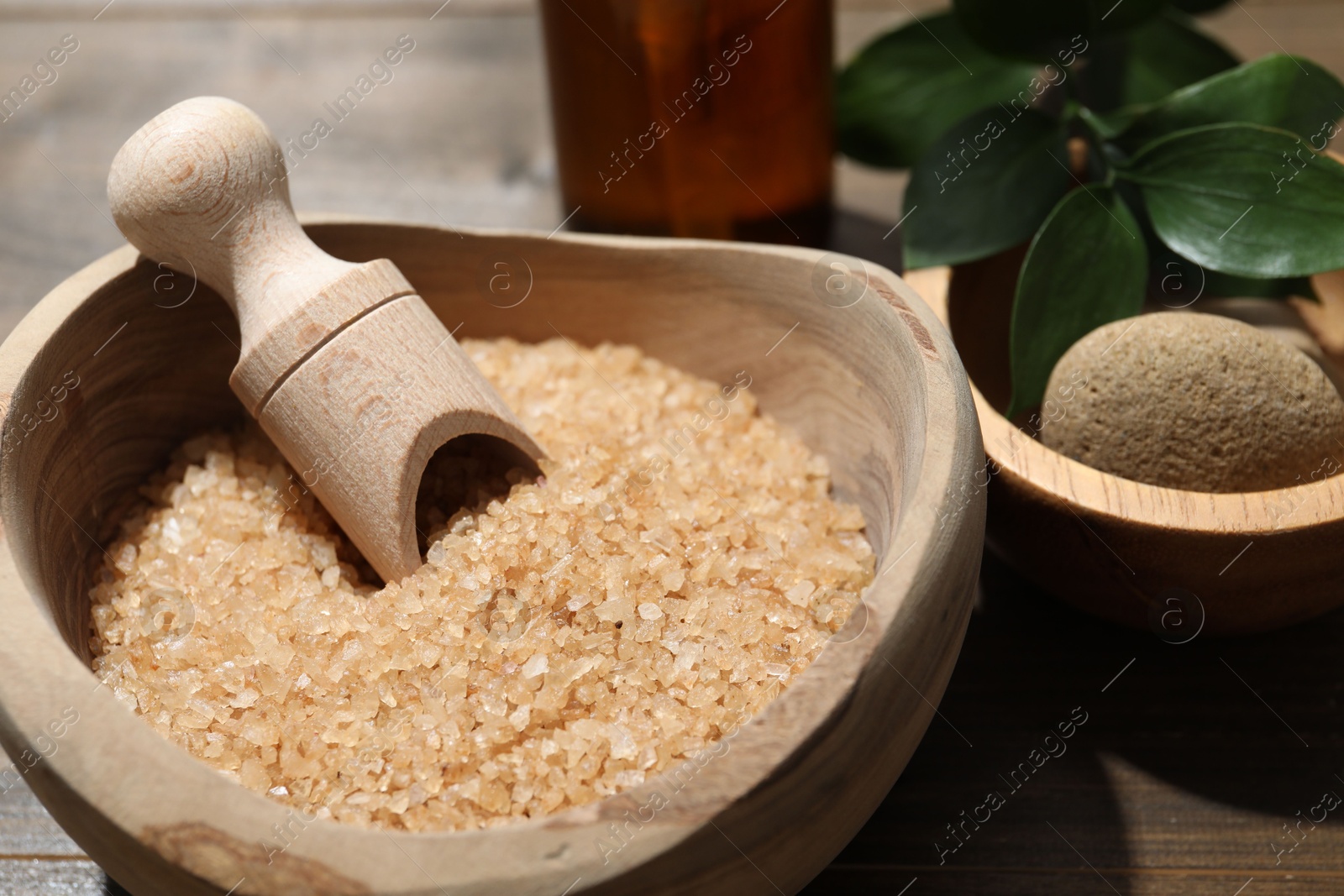 Photo of Bowl with sea salt and leaves on wooden table, closeup. Spa treatment