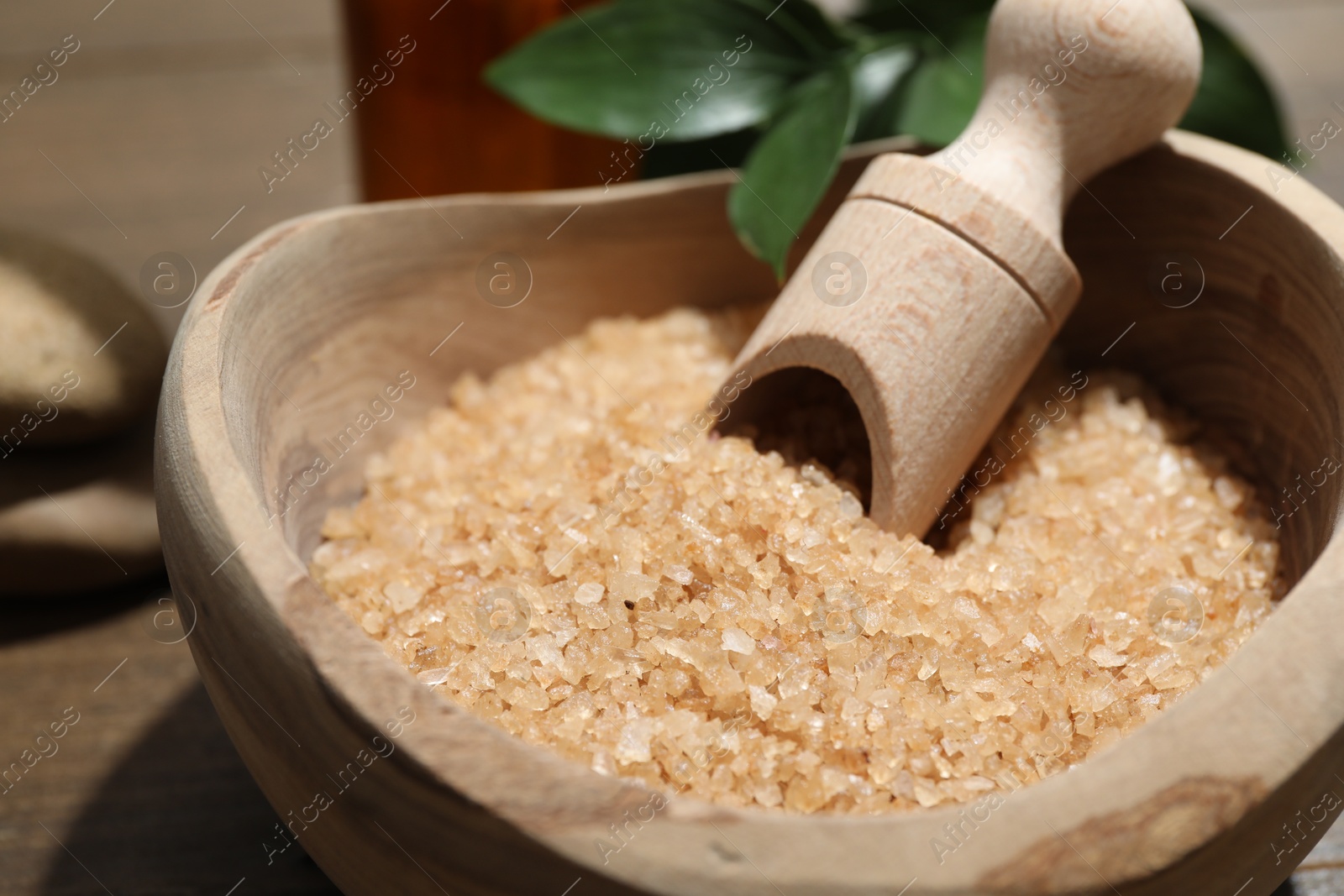 Photo of Bowl with sea salt and leaves on wooden table, closeup. Spa treatment