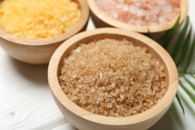 Spa composition with different types of sea salt on white wooden table, closeup