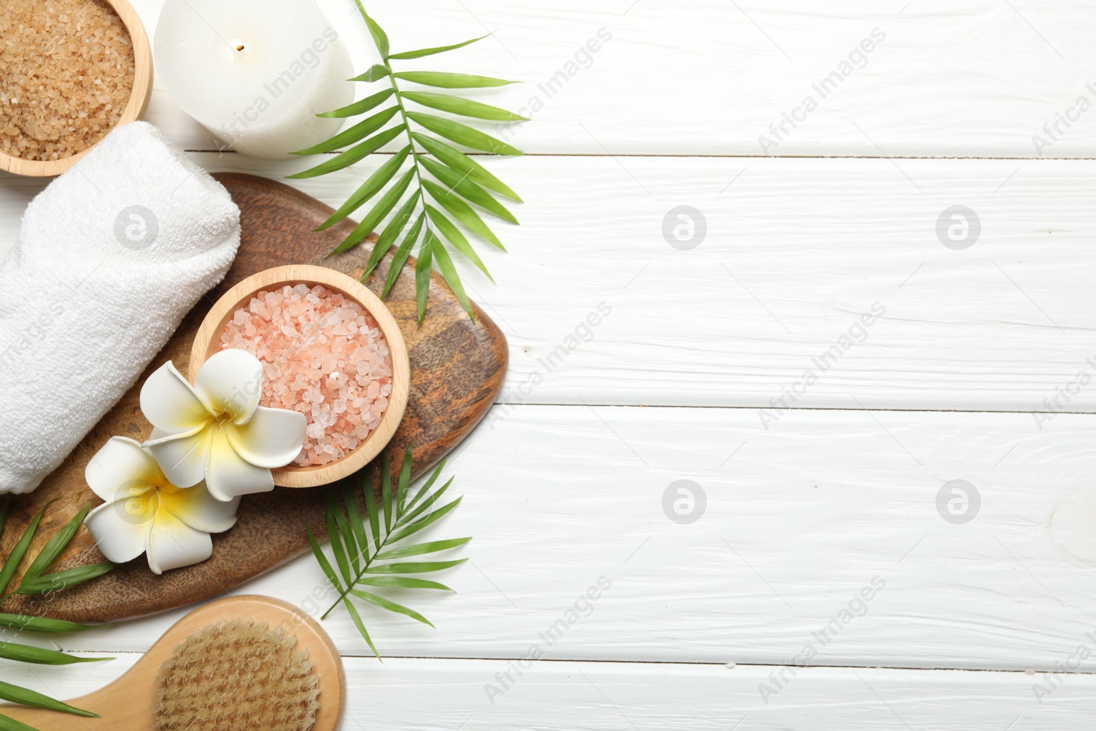 Photo of Spa composition with sea salt, plumeria flowers and burning candle on white wooden table, flat lay. Space for text