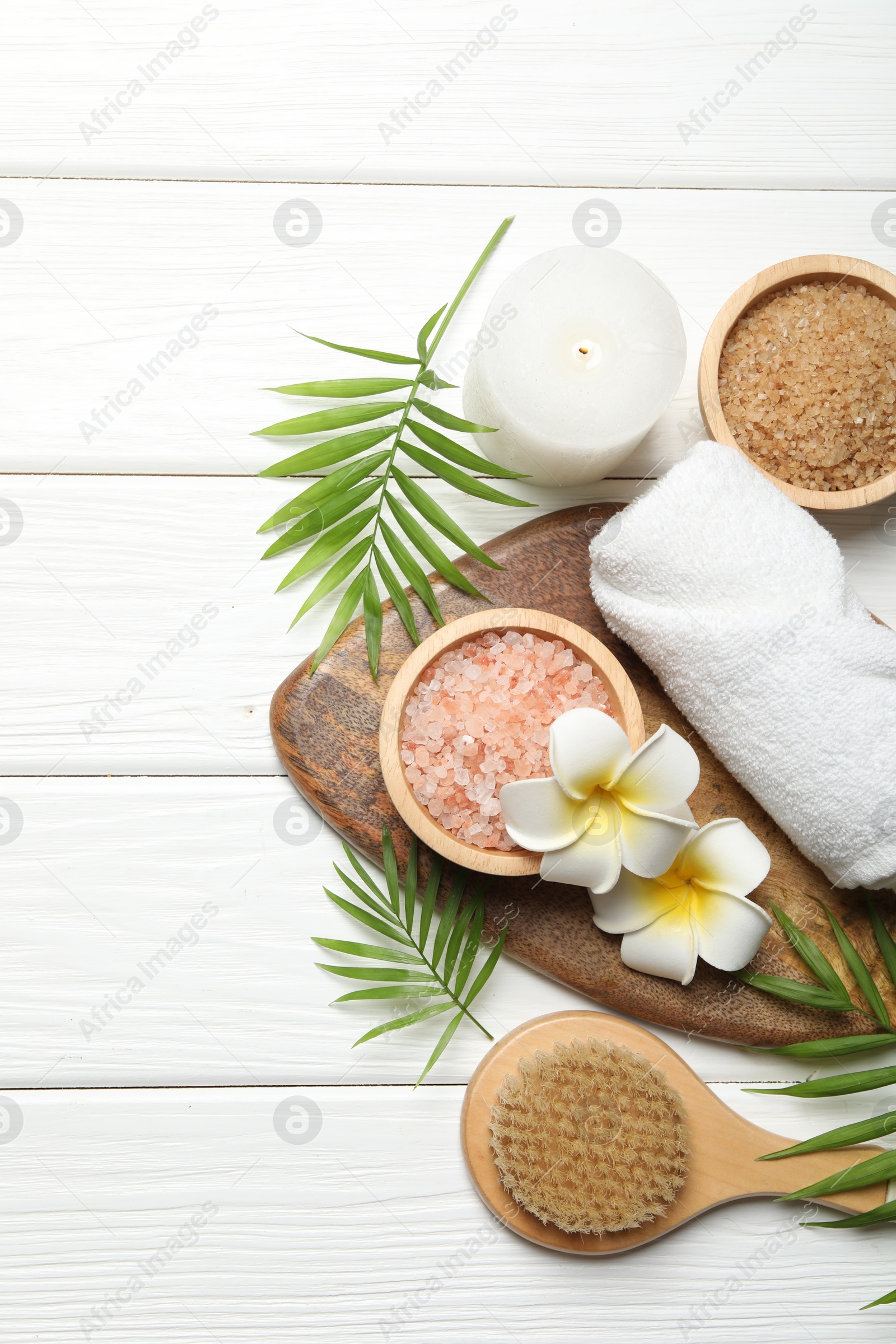 Photo of Spa composition with sea salt, plumeria flowers and burning candle on white wooden table, flat lay