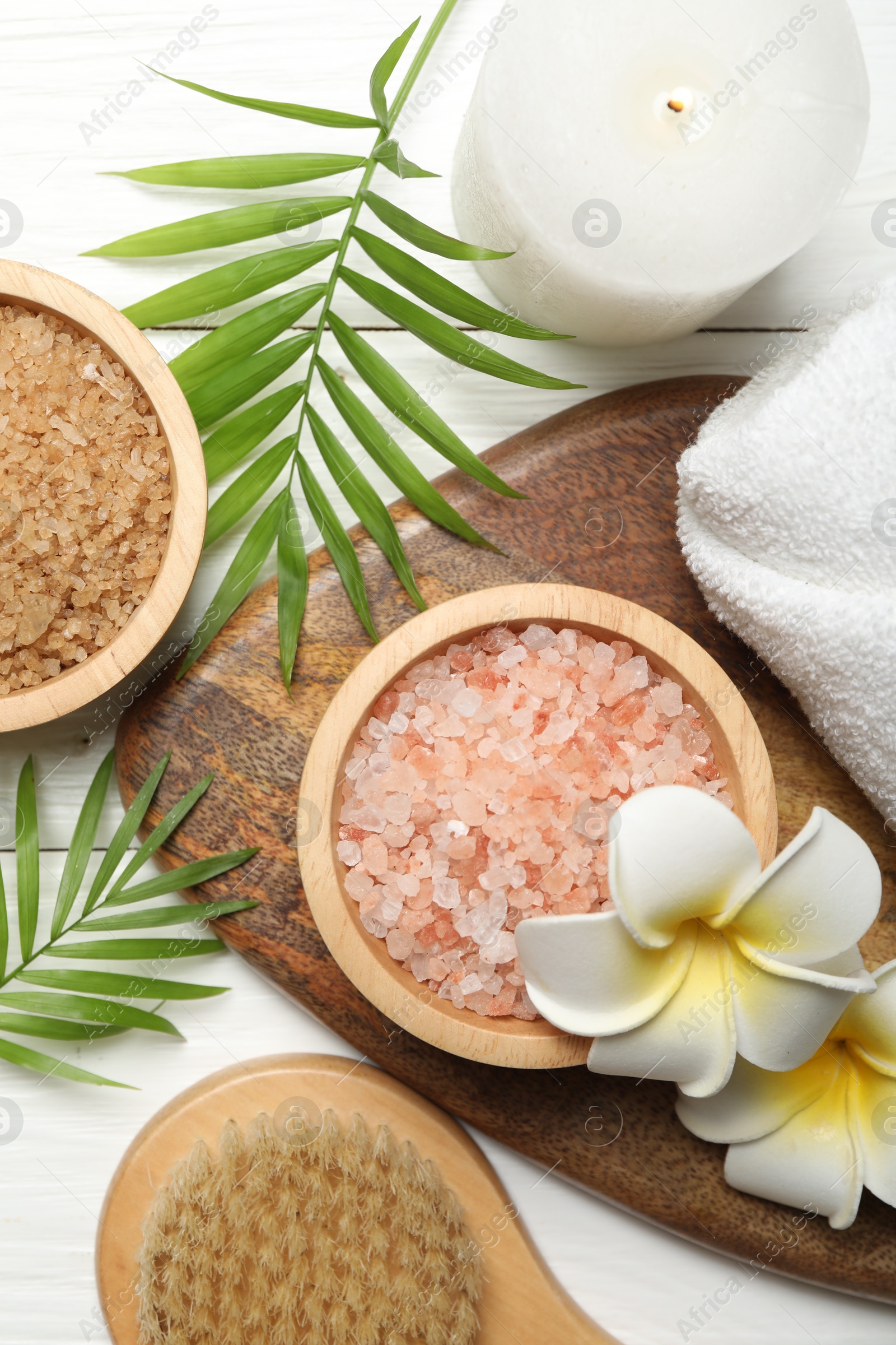 Photo of Spa composition with sea salt, plumeria flowers and burning candle on white wooden table, flat lay