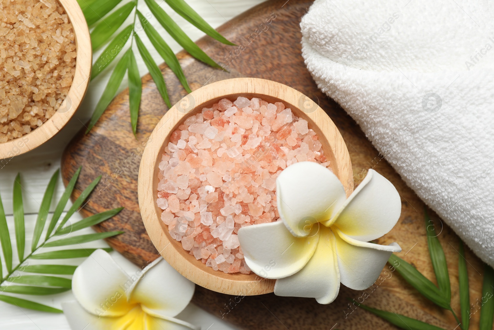 Photo of Spa composition with sea salt, plumeria flowers and towel on white wooden table, flat lay