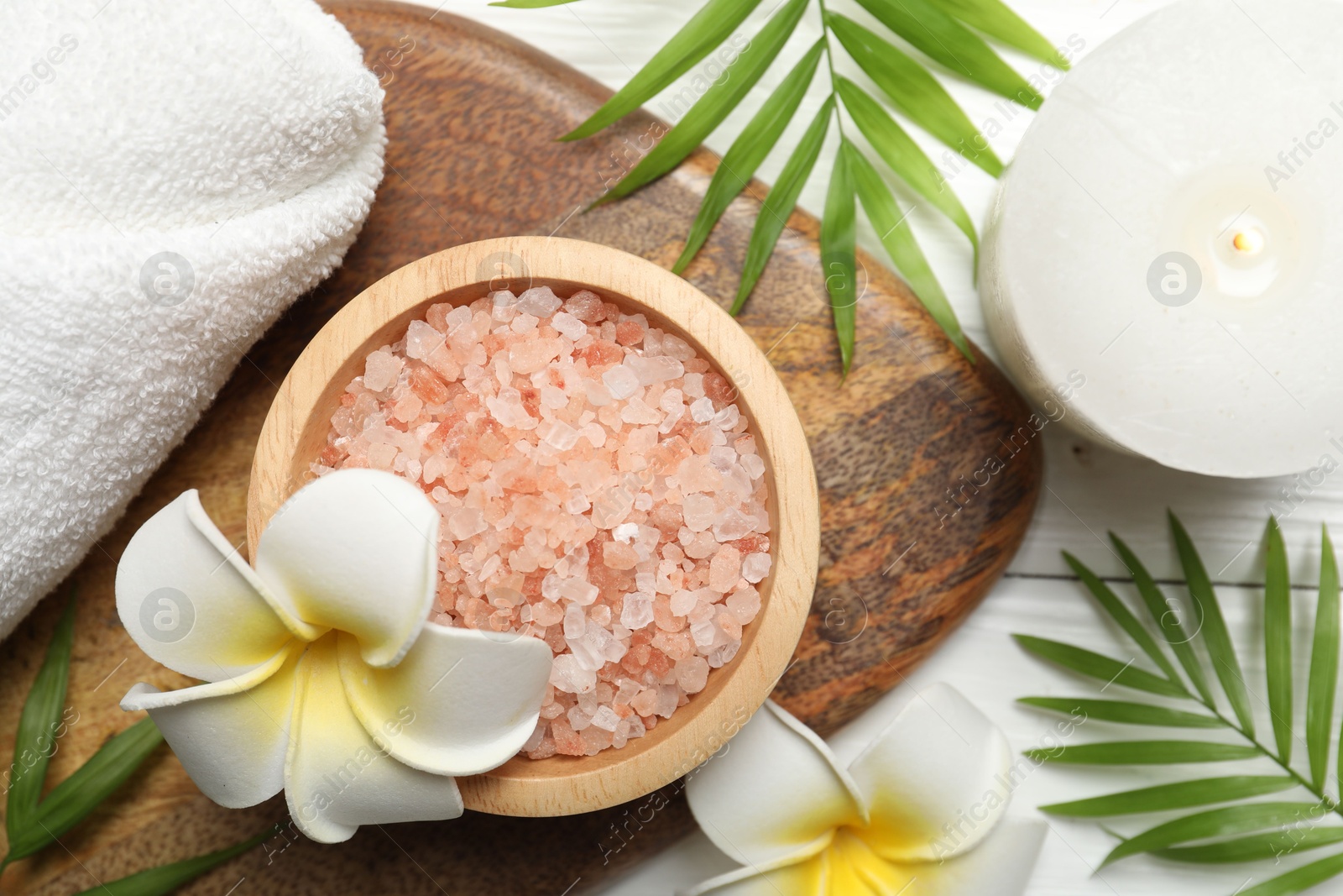 Photo of Spa composition with sea salt, plumeria flowers and burning candle on white wooden table, flat lay