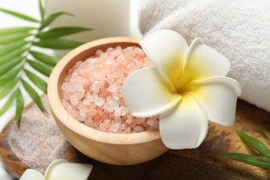 Photo of Spa composition with sea salt, plumeria flowers and towel on white wooden table, closeup