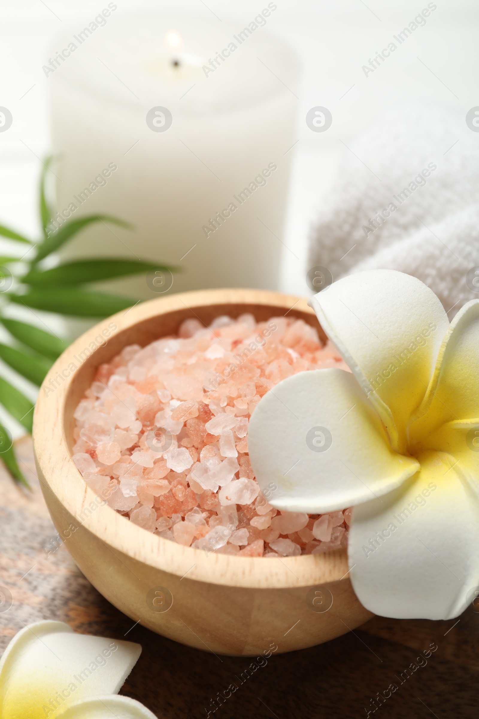 Photo of Spa composition with sea salt, plumeria flowers and burning candle on table, closeup