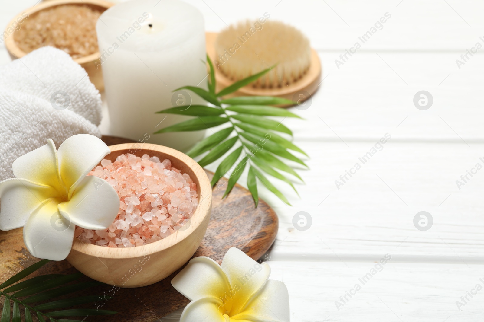 Photo of Spa composition with sea salt, plumeria flowers and burning candle on white wooden table, closeup. Space for text