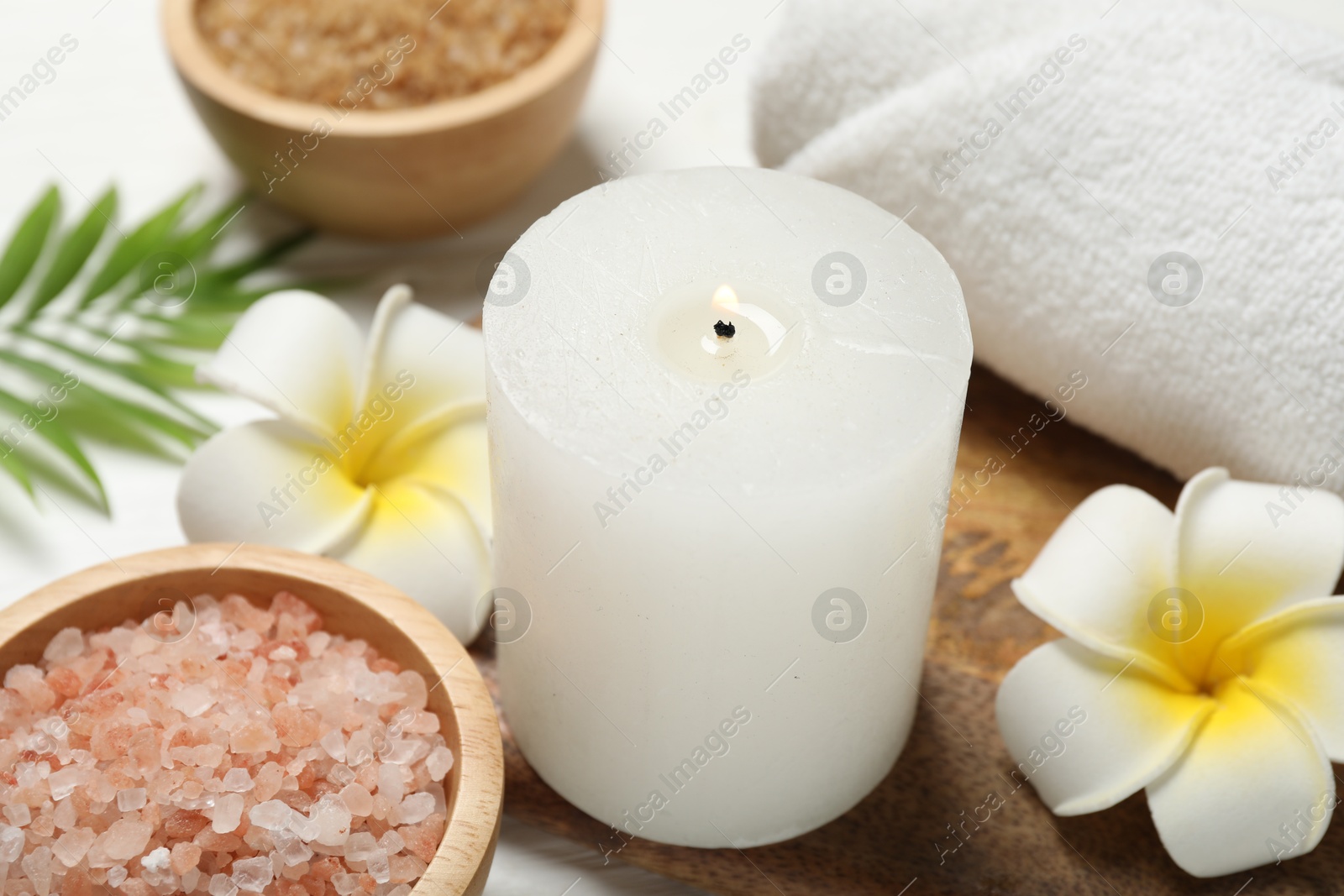 Photo of Spa composition with sea salt, plumeria flowers and burning candle on white wooden table, closeup