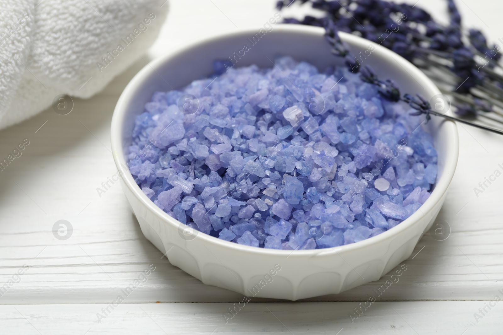 Photo of Bowl with sea salt, towel and lavender flowers on white wooden table. Spa treatment