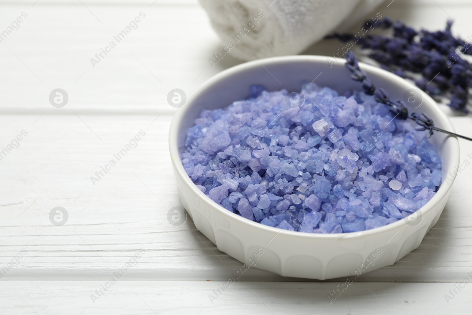 Photo of Bowl with sea salt, towel and lavender flowers on white wooden table. Spa treatment