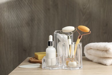 Face rollers, bottle of cosmetic product and towel on wooden table