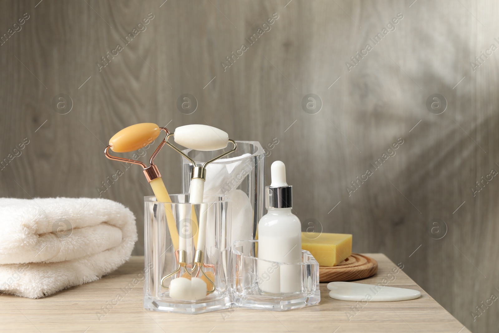 Photo of Face rollers, bottle of cosmetic product and towel on wooden table