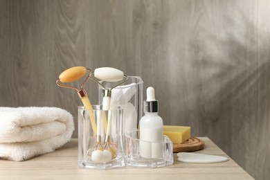 Photo of Face rollers, bottle of cosmetic product and towel on wooden table