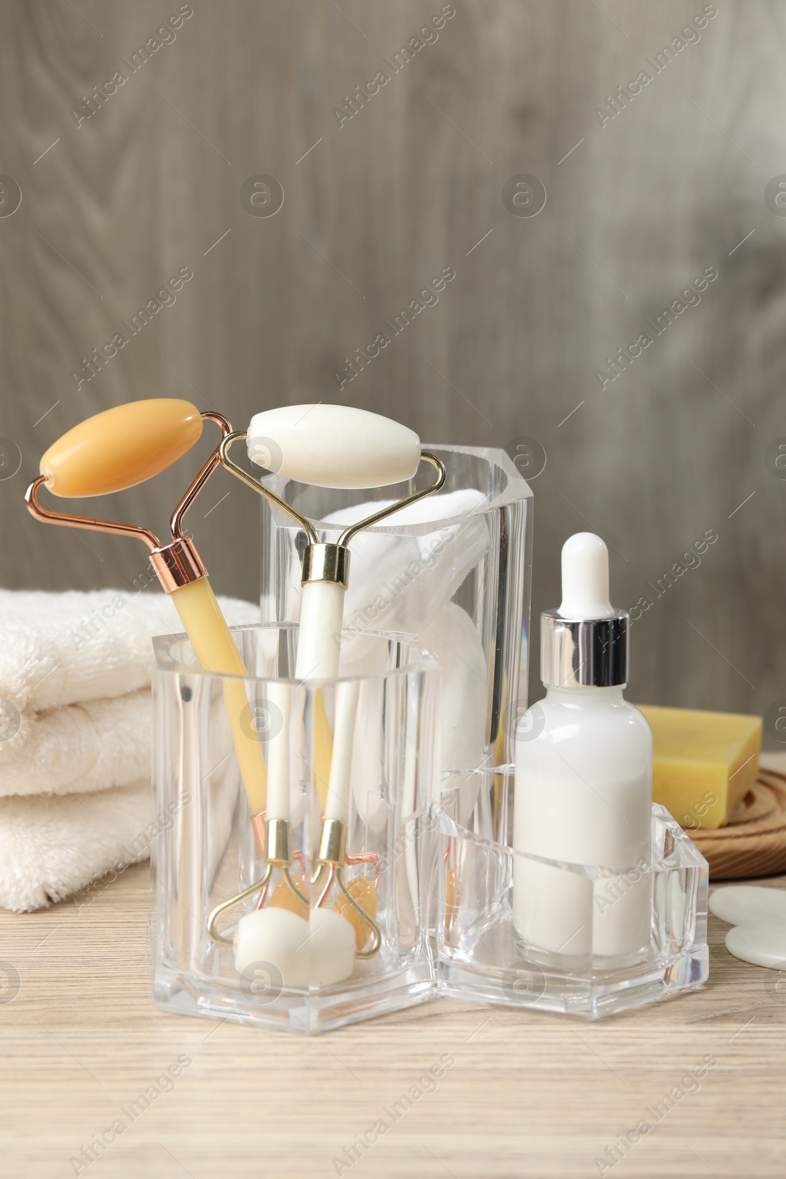 Photo of Face rollers, bottle of cosmetic product and towel on wooden table