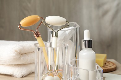 Face rollers, bottle of cosmetic product and towel on table, closeup