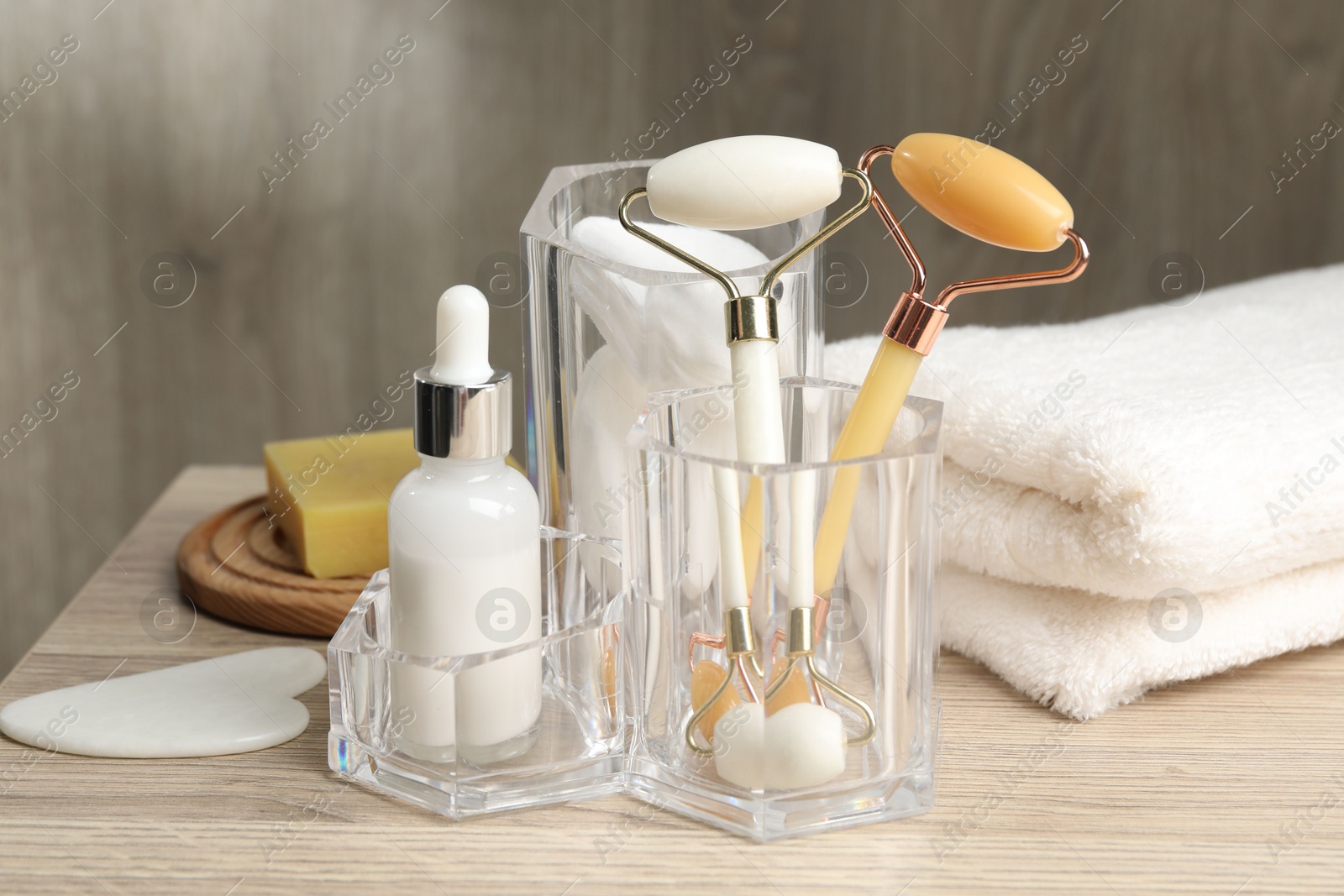 Photo of Face rollers, bottle of cosmetic product and towel on wooden table