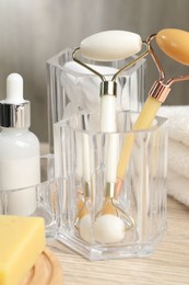 Photo of Face rollers, bottle of cosmetic product and towel on wooden table, closeup