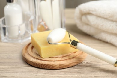 Face roller, soap and towel on wooden table, closeup