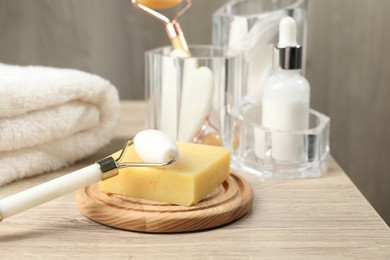 Face roller, soap and towel on wooden table, closeup