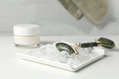 Face roller and ice cubes on white table, closeup