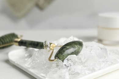 Face roller and ice cubes on white table, closeup