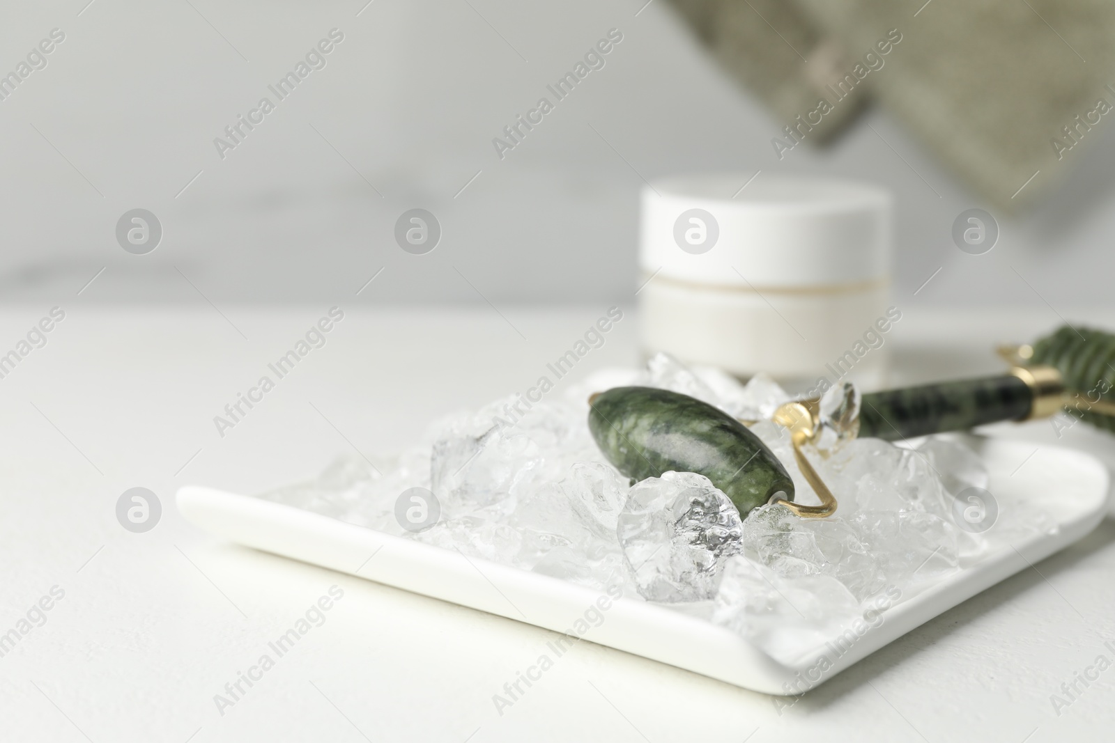 Photo of Face roller and ice cubes on white table, closeup. Space for text