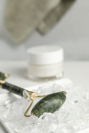 Face roller and ice cubes on white table, closeup