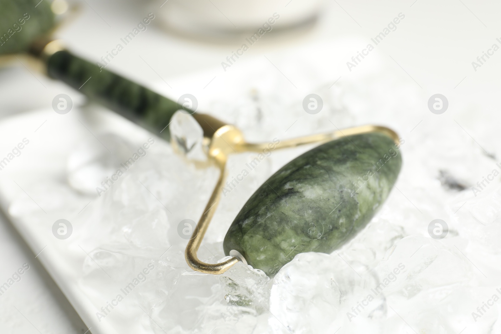 Photo of Face roller and ice cubes on white table, closeup