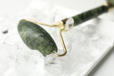 Face roller and ice cubes on white table, closeup