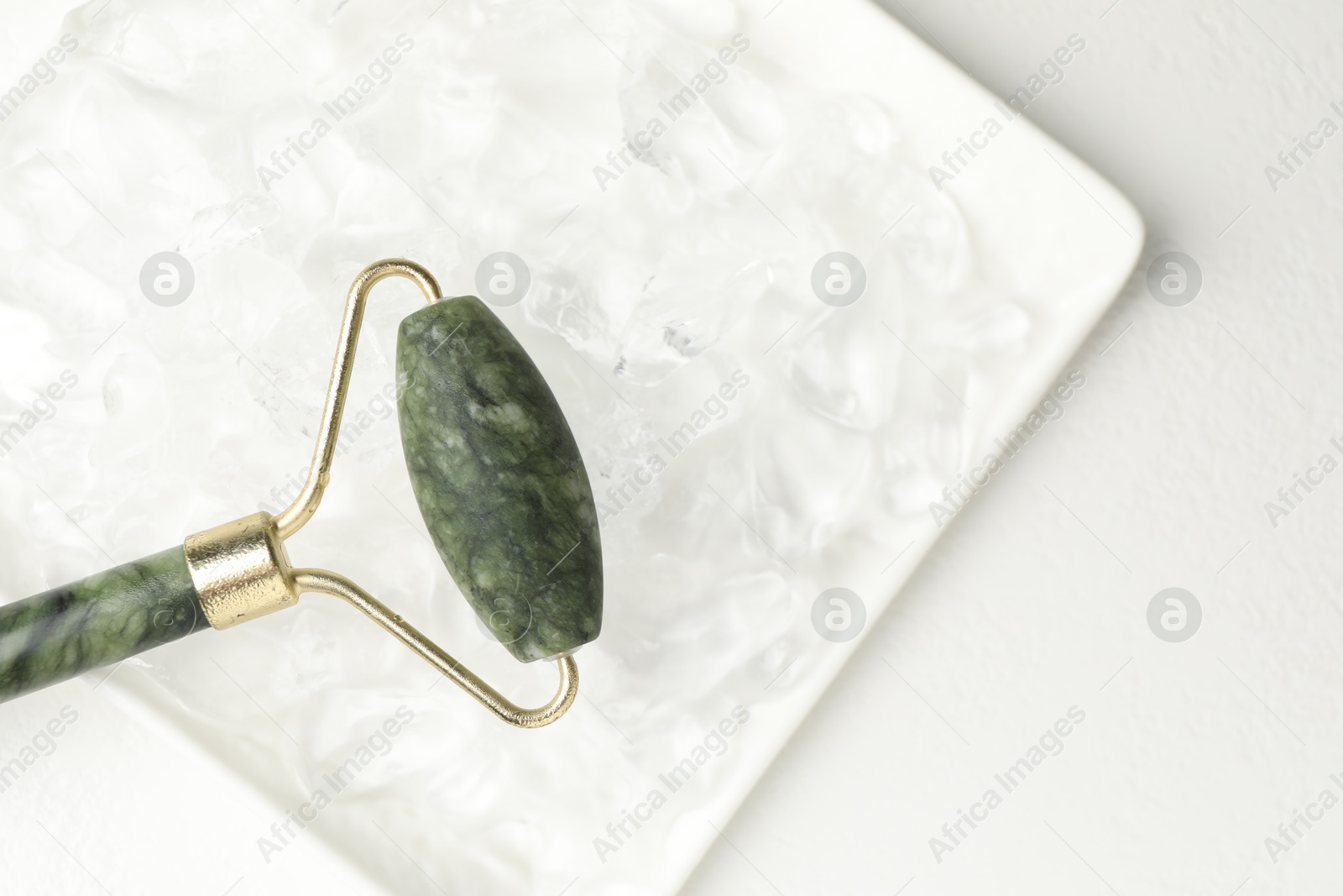 Photo of Face roller and ice cubes on white table, top view