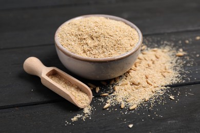 Photo of Oat bran in bowl, grains and scoop on black wooden table, closeup