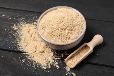 Oat bran in bowl, grains and scoop on black wooden table