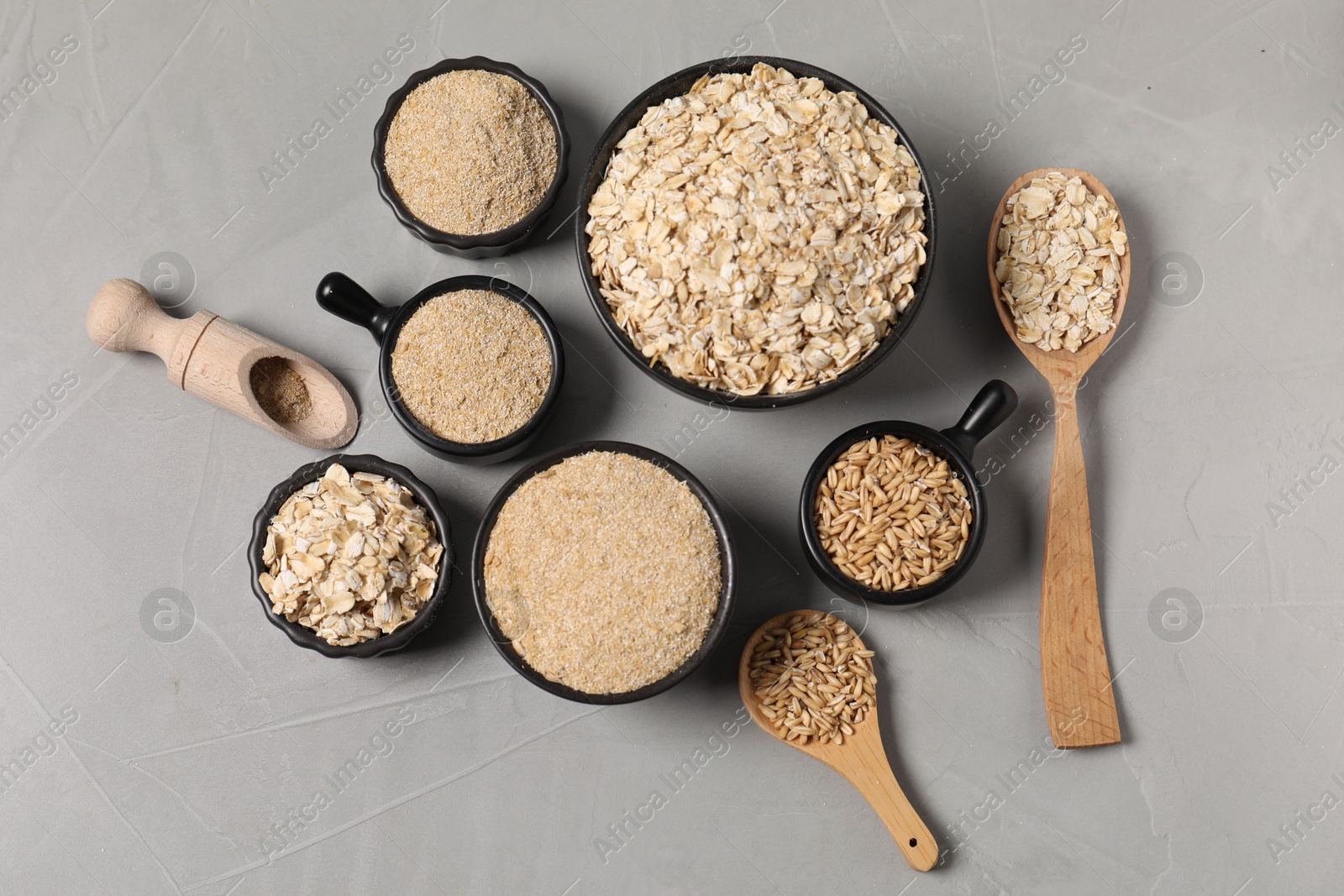 Photo of Oat bran, flakes and grains on grey table, flat lay