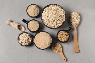 Photo of Oat bran, flakes and grains on grey table, flat lay