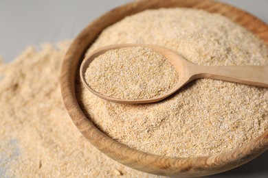 Photo of Oat bran in bowl and wooden spoon on table, closeup