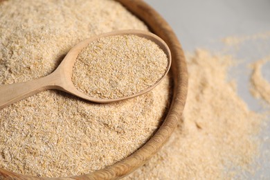 Photo of Oat bran in bowl and wooden spoon on table, closeup