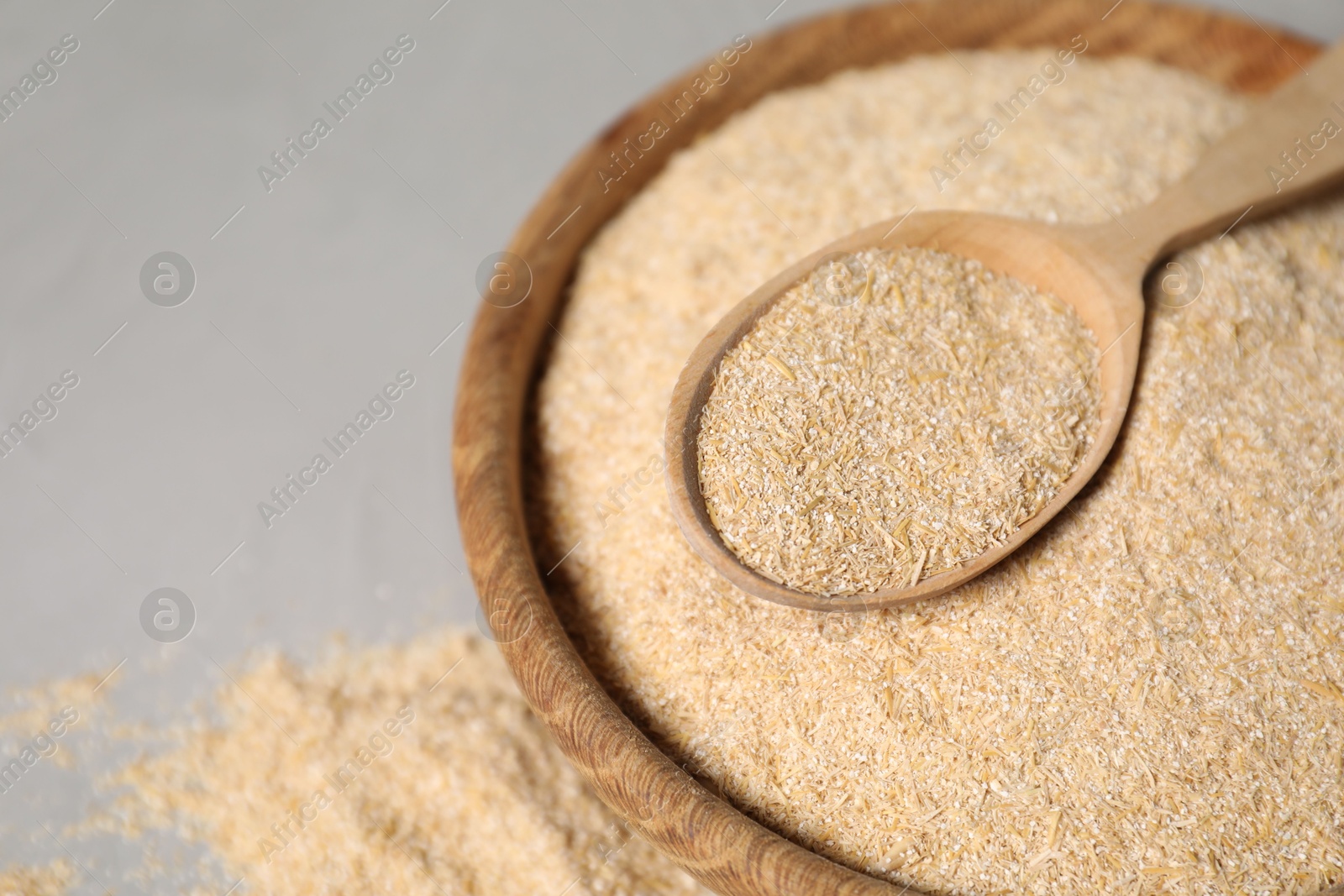 Photo of Oat bran in bowl and wooden spoon on grey table, closeup