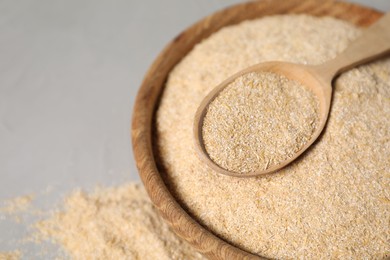 Photo of Oat bran in bowl and wooden spoon on grey table, closeup