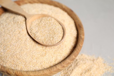 Photo of Oat bran in bowl and wooden spoon on grey table, closeup