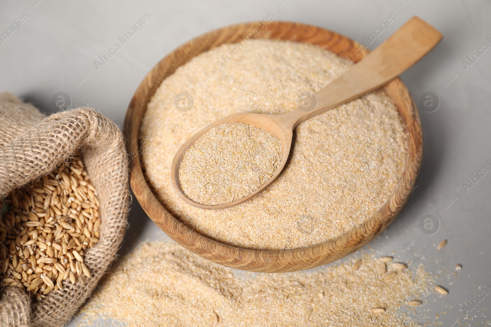 Photo of Oat bran in bowl, spoon and burlap bag with grains on grey table, closeup