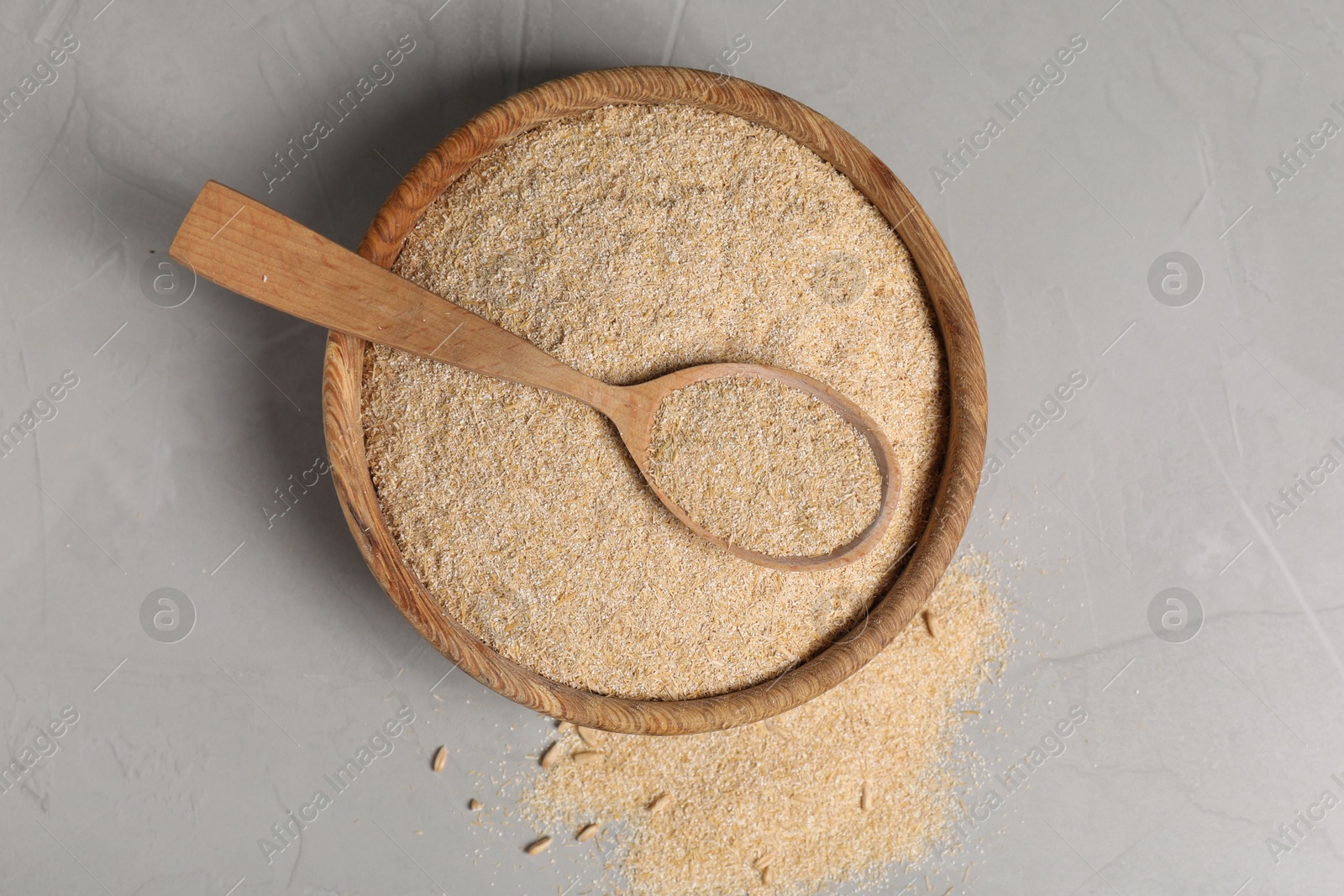 Photo of Oat bran in bowl and wooden spoon on grey table, top view