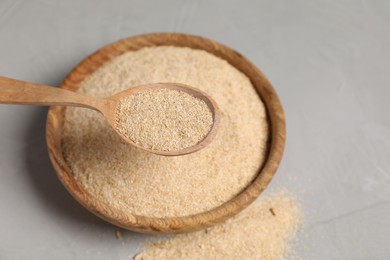 Photo of Oat bran in wooden spoon over bowl at grey table, closeup