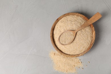 Photo of Oat bran in bowl and wooden spoon on grey table, top view. Space for text