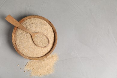 Photo of Oat bran in bowl and wooden spoon on grey table, top view. Space for text