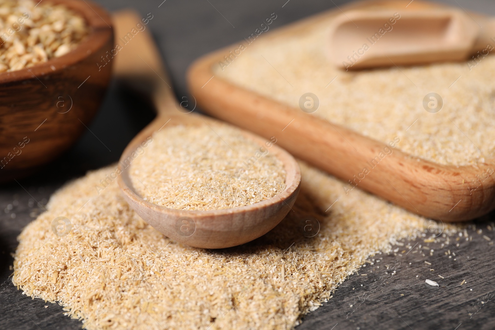 Photo of Oat bran in wooden spoon and grains on grey table, closeup