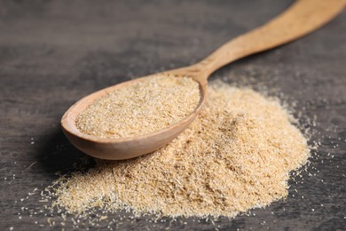 Photo of Oat bran in wooden spoon on grey table, closeup