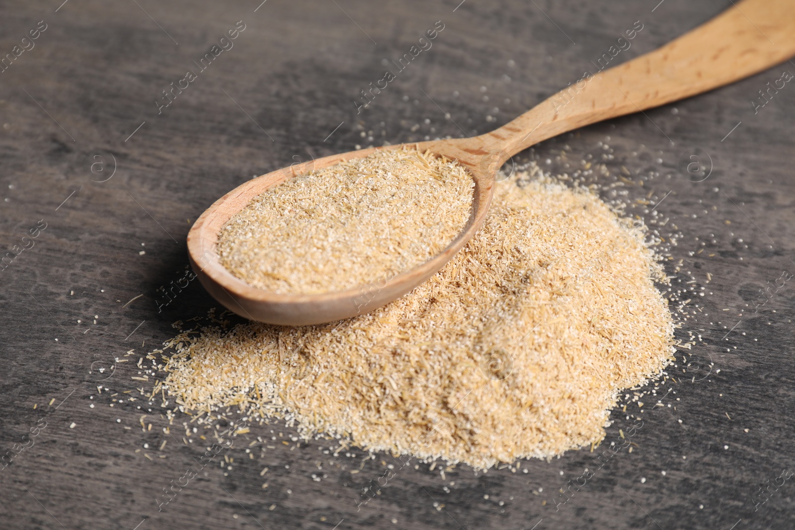 Photo of Oat bran in wooden spoon on grey table, closeup