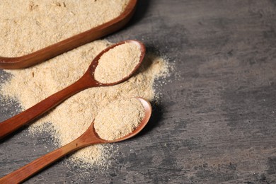 Photo of Oat bran in wooden spoons on grey table, closeup. Space for text