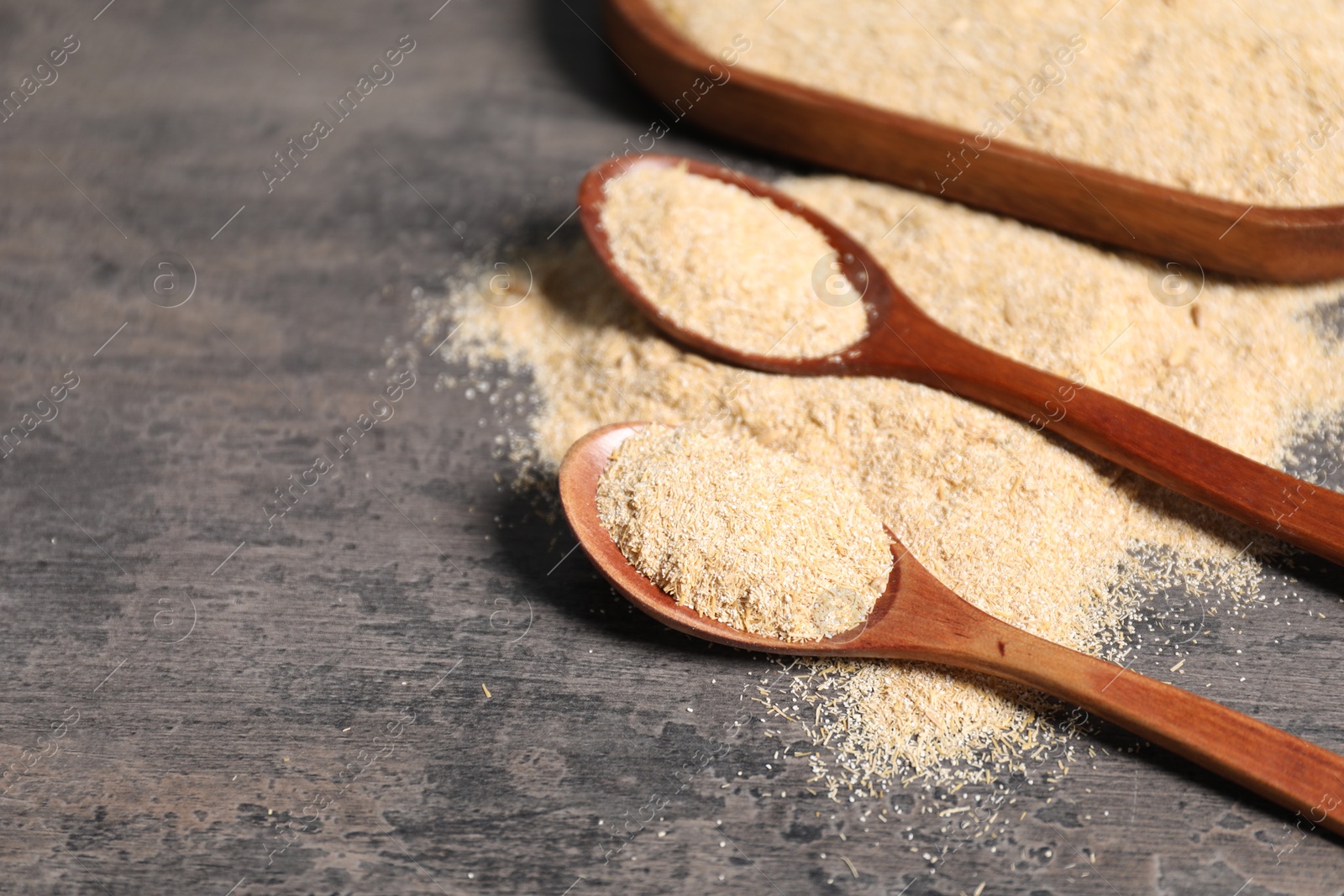 Photo of Oat bran in wooden spoons on grey table, closeup. Space for text