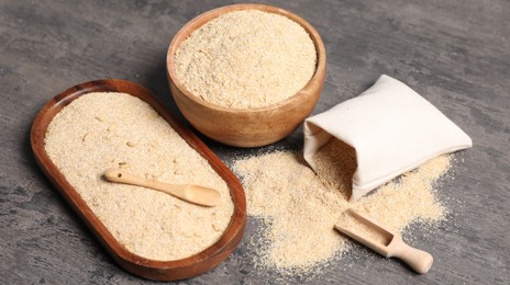 Photo of Oat bran in bowl, spoon, scoop and burlap bag on grey table